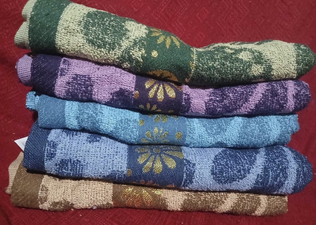 Toalhas Belora dobradas e empilhadas em verde, lilás, azul e marrom